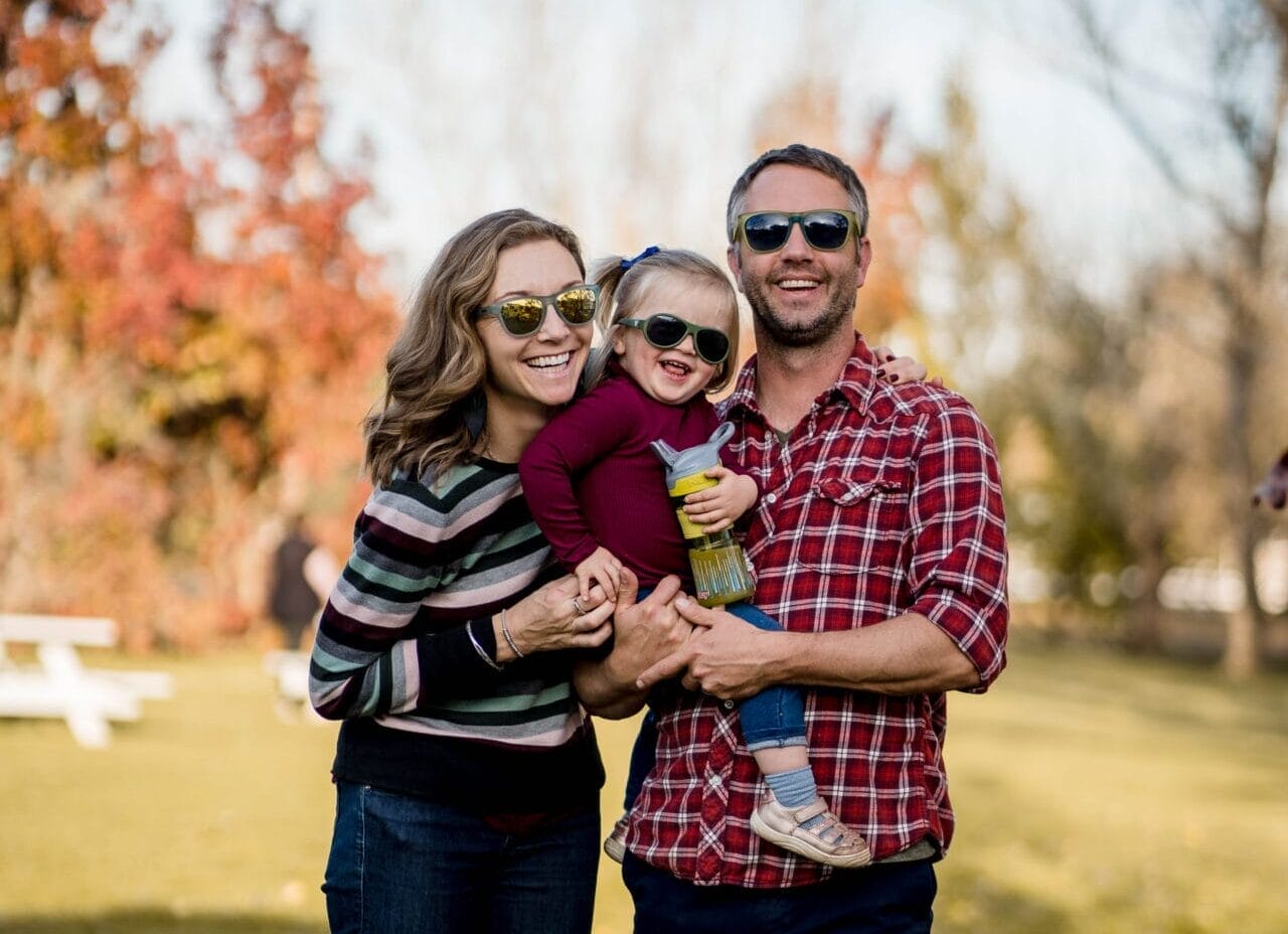 A family of three posing for a photo in the park with sunglasses on
